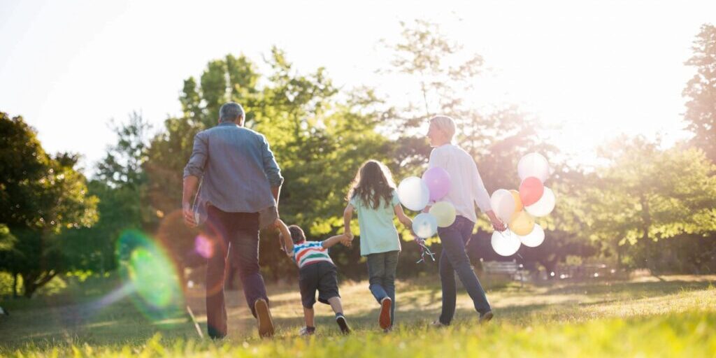 A family is walking in the grass with balloons.